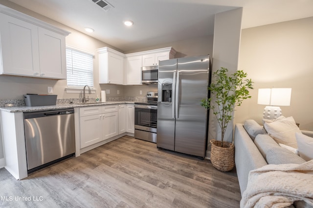 kitchen with light stone countertops, appliances with stainless steel finishes, sink, light hardwood / wood-style flooring, and white cabinetry