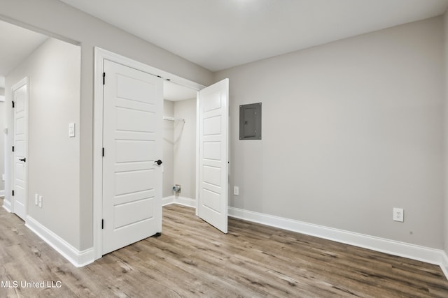 unfurnished bedroom featuring a barn door, electric panel, a closet, and light hardwood / wood-style floors