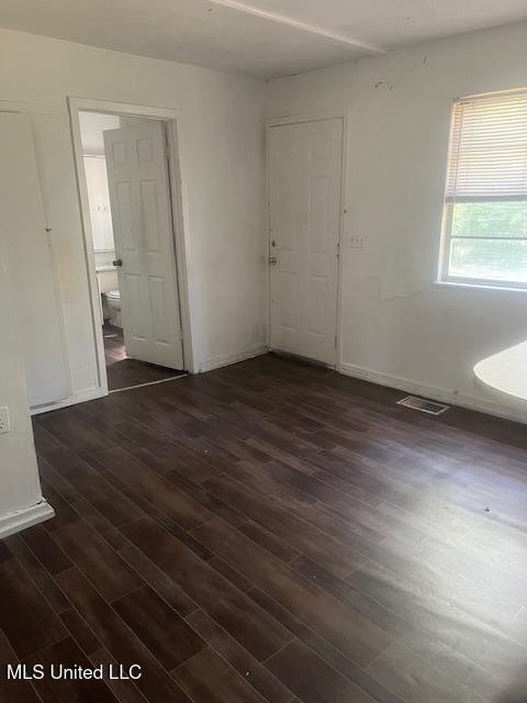 empty room with dark wood finished floors, visible vents, and baseboards