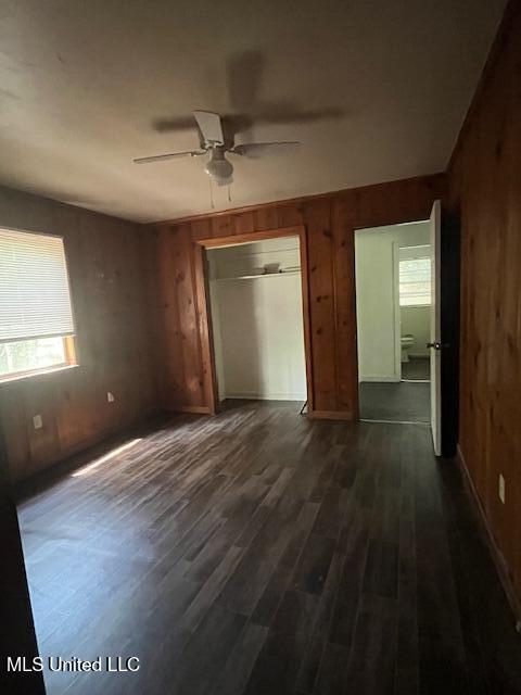 interior space featuring wood walls, ceiling fan, dark wood-style floors, and a closet