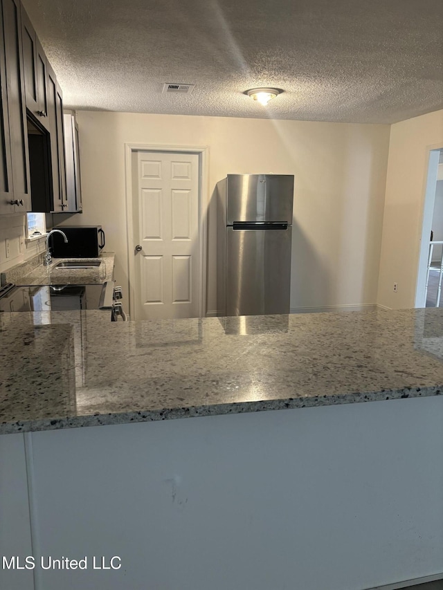 kitchen with light stone countertops, a textured ceiling, and stainless steel refrigerator