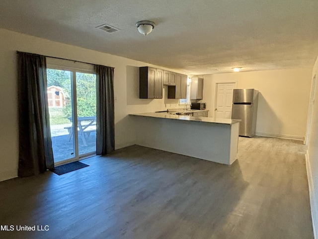 kitchen with light hardwood / wood-style flooring, stainless steel refrigerator, gray cabinetry, a textured ceiling, and kitchen peninsula