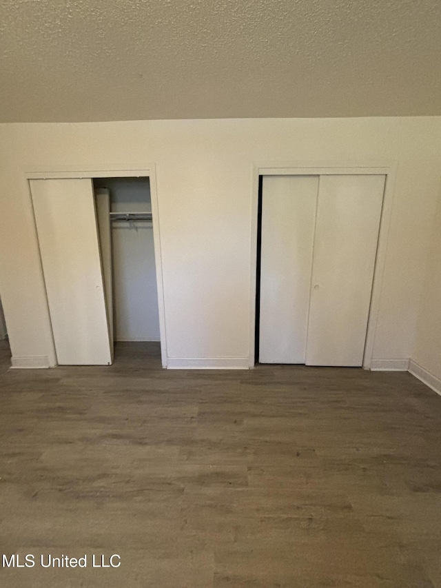 unfurnished bedroom featuring dark hardwood / wood-style floors, a textured ceiling, and two closets