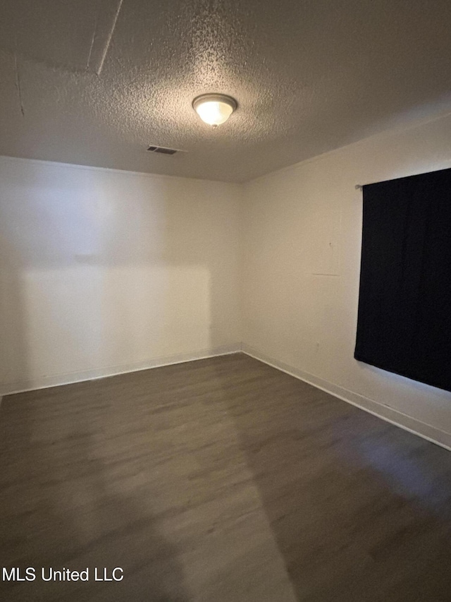 empty room with dark hardwood / wood-style floors and a textured ceiling