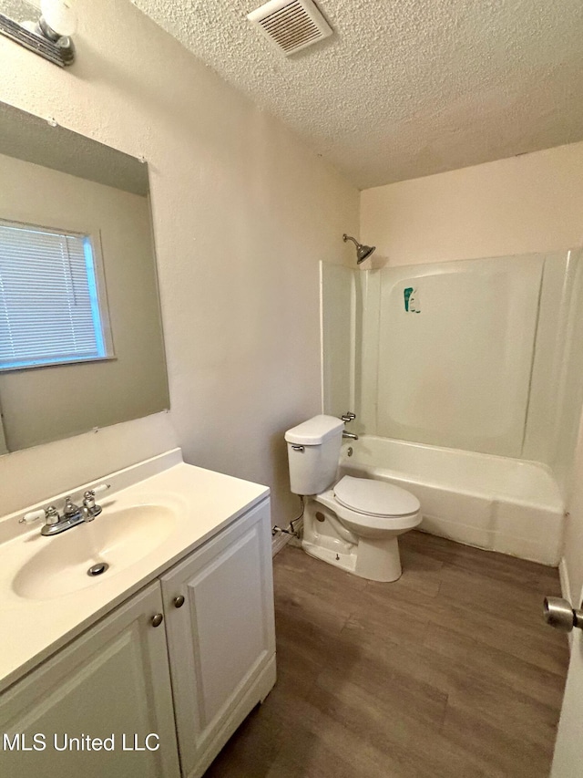 full bathroom featuring hardwood / wood-style flooring, vanity, shower / bath combination, toilet, and a textured ceiling