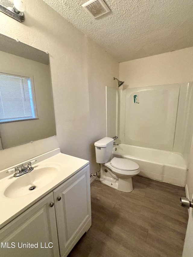 full bathroom with hardwood / wood-style floors, vanity, toilet, bathing tub / shower combination, and a textured ceiling