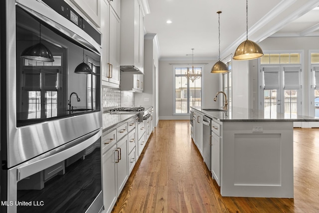 kitchen featuring appliances with stainless steel finishes, an island with sink, hanging light fixtures, and white cabinets