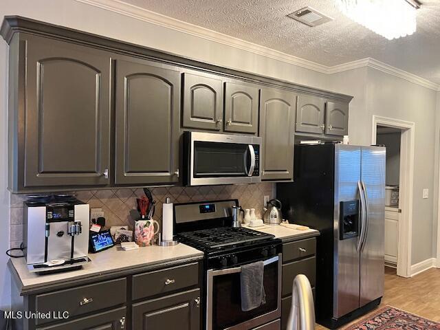 kitchen featuring hardwood / wood-style floors, appliances with stainless steel finishes, crown molding, decorative backsplash, and a textured ceiling