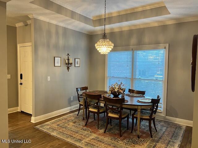 dining space with a chandelier, a tray ceiling, crown molding, and dark wood-type flooring