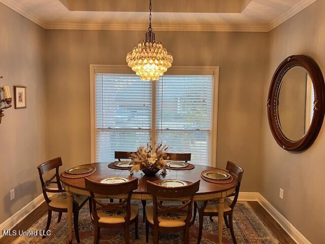 dining space with dark hardwood / wood-style flooring, an inviting chandelier, a raised ceiling, and crown molding