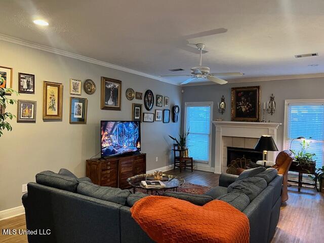 living room featuring crown molding, a fireplace, ceiling fan, and hardwood / wood-style flooring