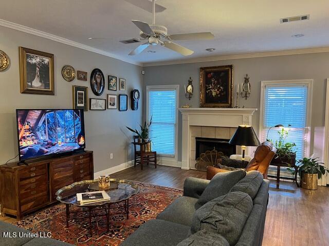 living room with a tile fireplace, ceiling fan, crown molding, and dark hardwood / wood-style floors