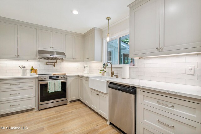 kitchen featuring tasteful backsplash, appliances with stainless steel finishes, light wood-type flooring, pendant lighting, and sink