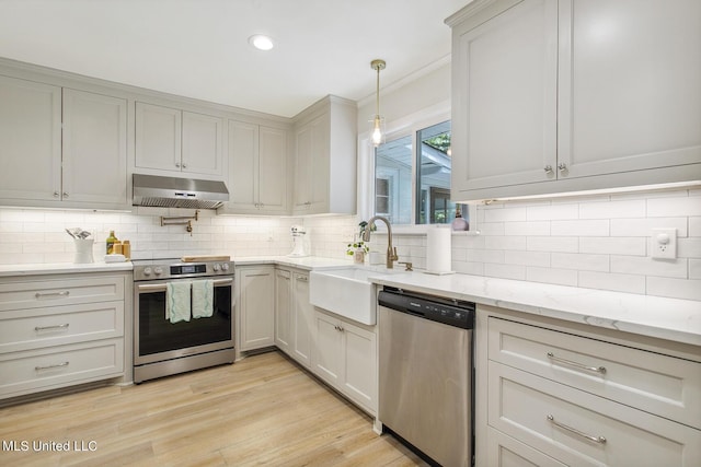 kitchen with a sink, backsplash, under cabinet range hood, appliances with stainless steel finishes, and ornamental molding
