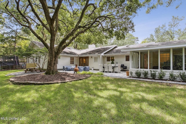 back of house featuring a yard, a trampoline, a patio area, and a chimney
