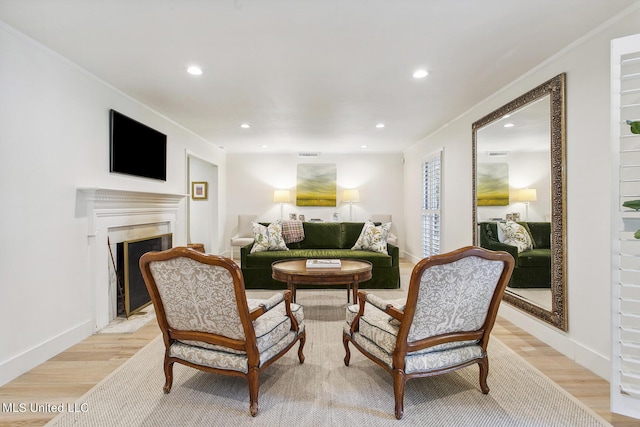 sitting room with a fireplace with flush hearth, light wood-type flooring, baseboards, ornamental molding, and recessed lighting