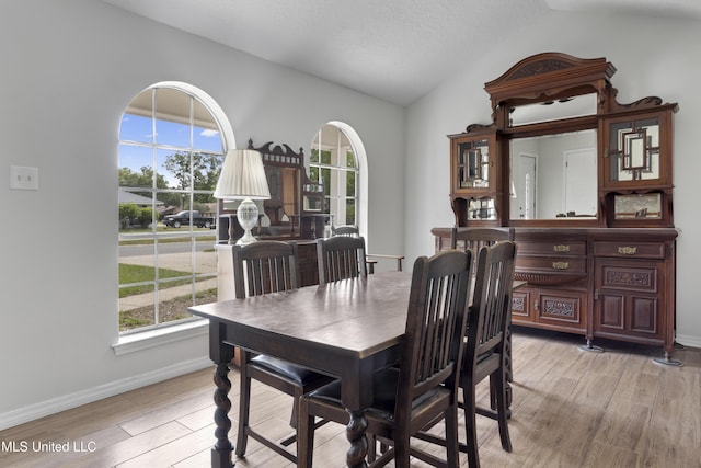 dining space with a healthy amount of sunlight, baseboards, light wood finished floors, and lofted ceiling