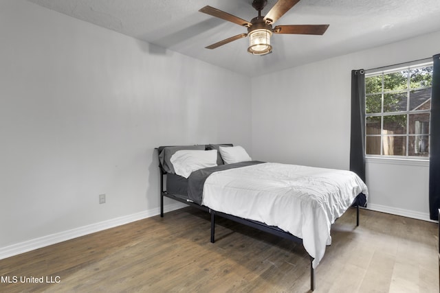 bedroom featuring baseboards, ceiling fan, a textured ceiling, and wood finished floors