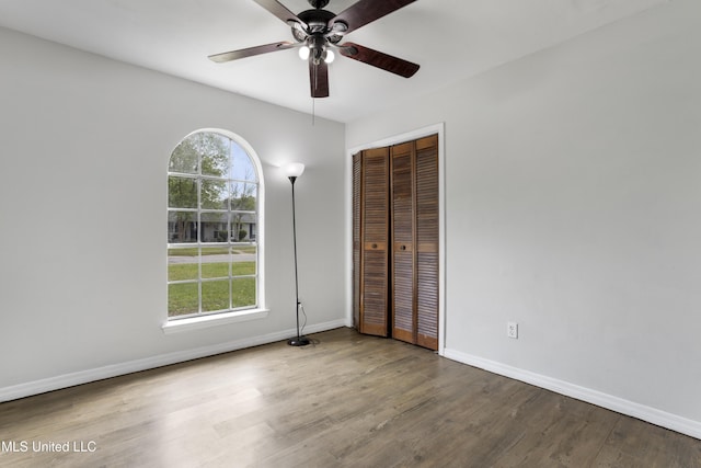 unfurnished bedroom featuring baseboards, multiple windows, wood finished floors, and a closet