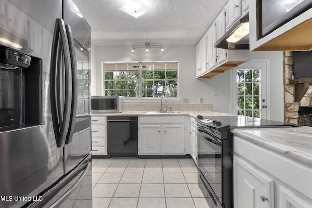 kitchen with light tile patterned flooring, light countertops, under cabinet range hood, a sink, and black appliances