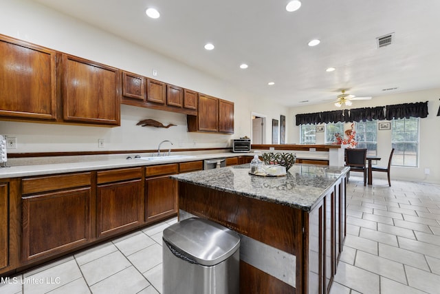 kitchen featuring sink, light tile patterned floors, a center island, light stone countertops, and stainless steel dishwasher