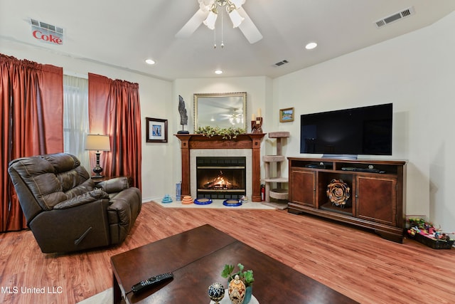 living room with a tiled fireplace, wood-type flooring, and ceiling fan