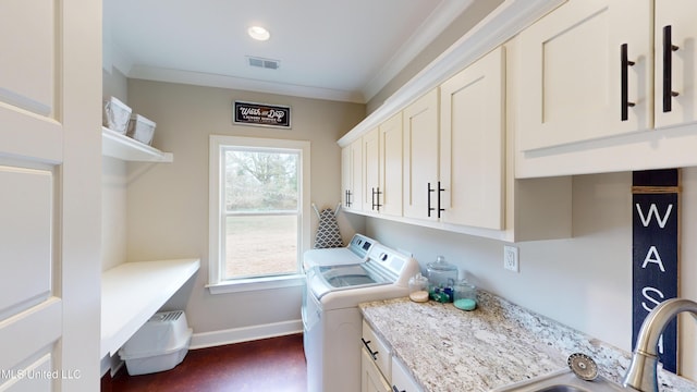 clothes washing area featuring a wealth of natural light, crown molding, washing machine and clothes dryer, and cabinets