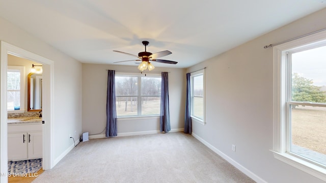 unfurnished bedroom with light carpet, ceiling fan, multiple windows, and ensuite bath