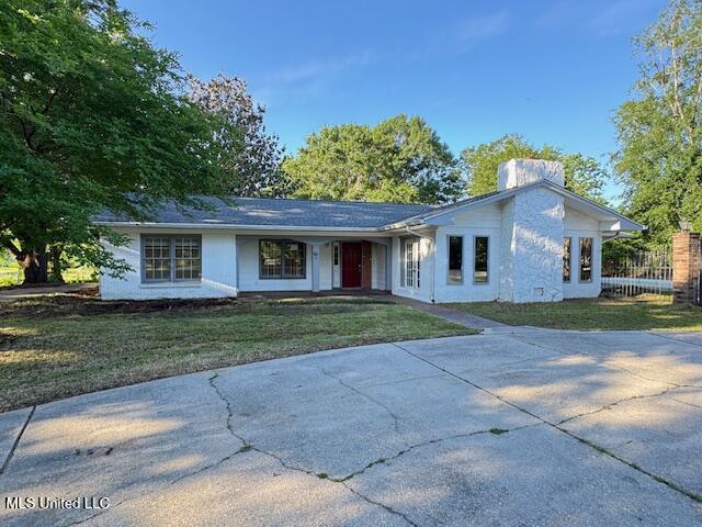 ranch-style house with concrete driveway, a chimney, and a front yard