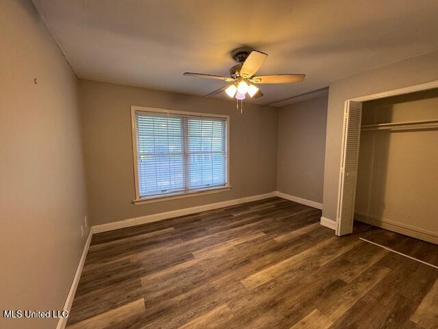 unfurnished bedroom featuring ceiling fan, baseboards, dark wood-type flooring, and a closet