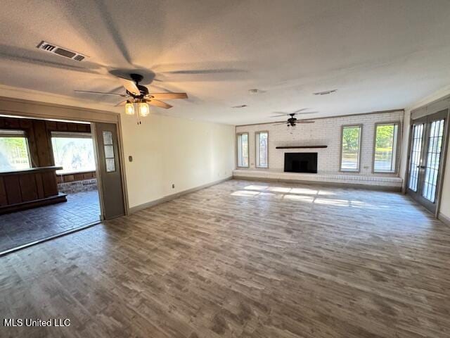unfurnished living room featuring wood finished floors, a brick fireplace, visible vents, baseboards, and ceiling fan