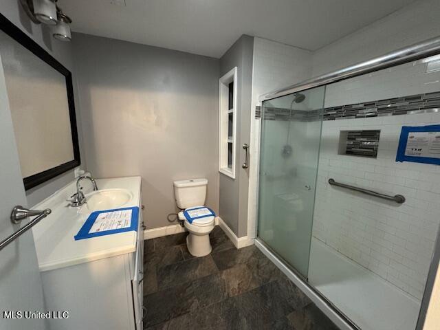 full bath with a stall shower, vanity, toilet, and baseboards