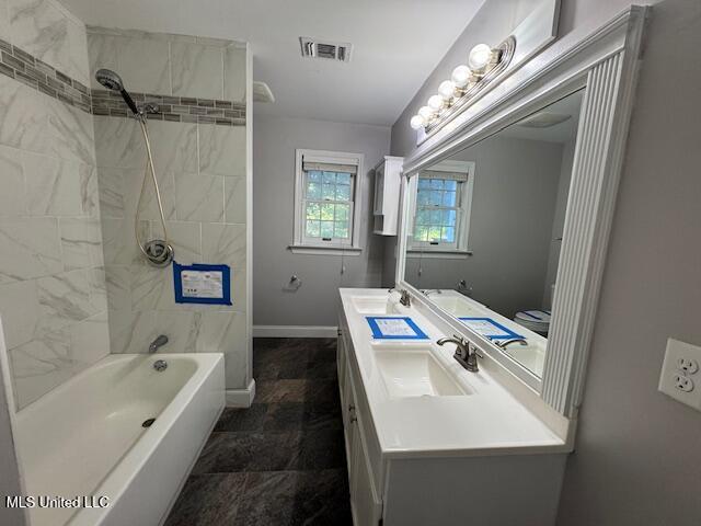 full bath with baseboards, visible vents, a sink, bathtub / shower combination, and double vanity