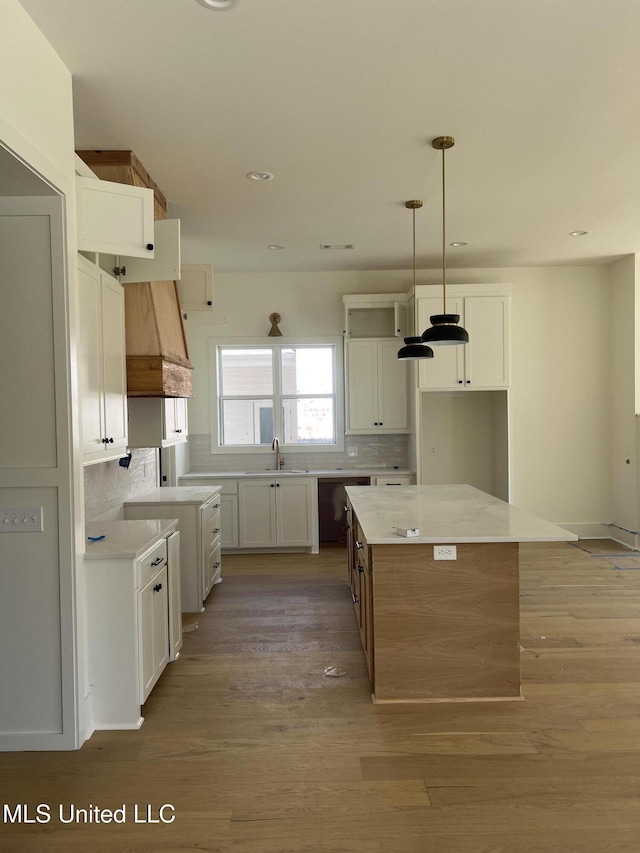 kitchen with tasteful backsplash, light wood-style flooring, premium range hood, and a sink