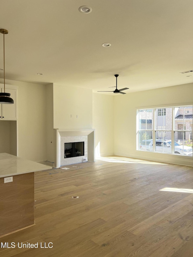 unfurnished living room with visible vents, a tiled fireplace, wood finished floors, recessed lighting, and ceiling fan