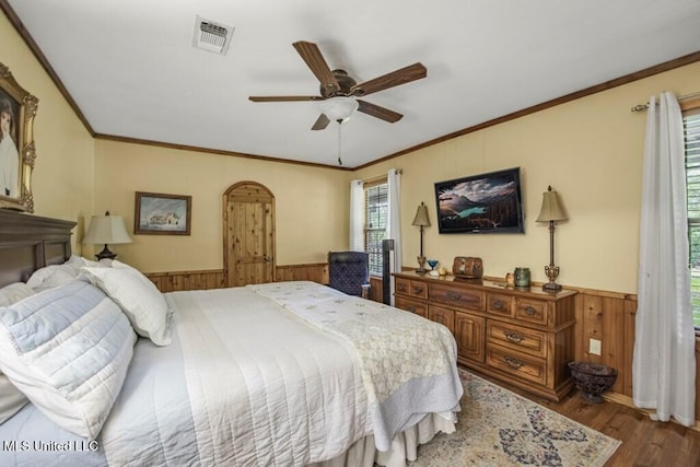 bedroom with ceiling fan, wooden walls, wood-type flooring, and ornamental molding