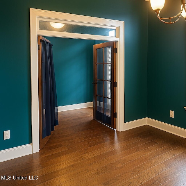 spare room featuring baseboards, wood finished floors, and a notable chandelier
