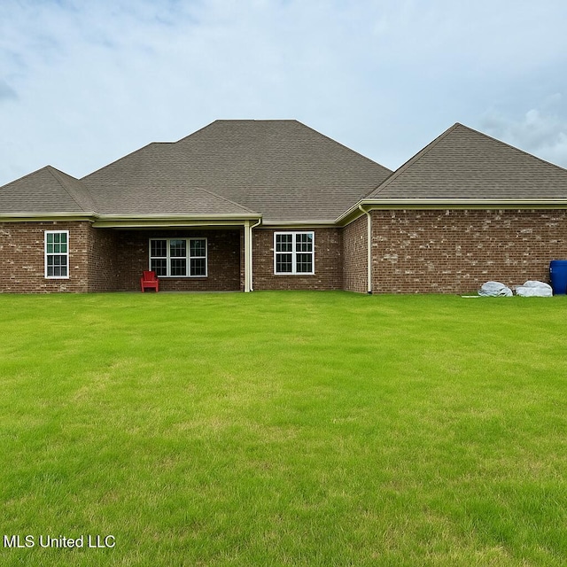 rear view of property with a lawn, a shingled roof, and brick siding
