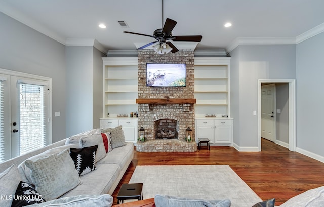 living room with crown molding, dark wood-type flooring, built in features, ceiling fan, and a fireplace