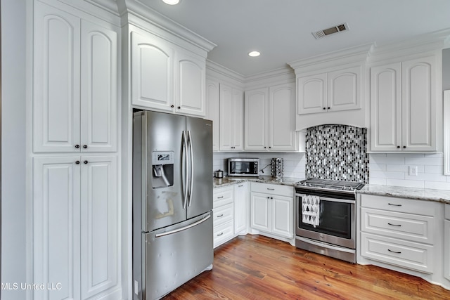 kitchen with hardwood / wood-style floors, tasteful backsplash, white cabinets, light stone counters, and stainless steel appliances