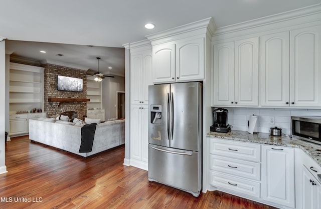 kitchen with white cabinetry, a brick fireplace, stainless steel appliances, and light stone countertops