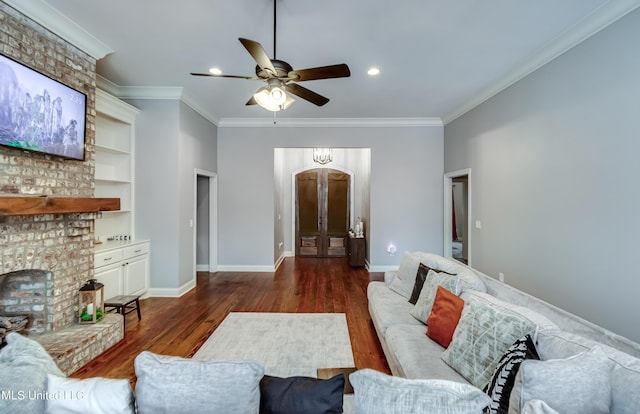 living room with a fireplace, dark hardwood / wood-style flooring, ceiling fan, crown molding, and built in shelves