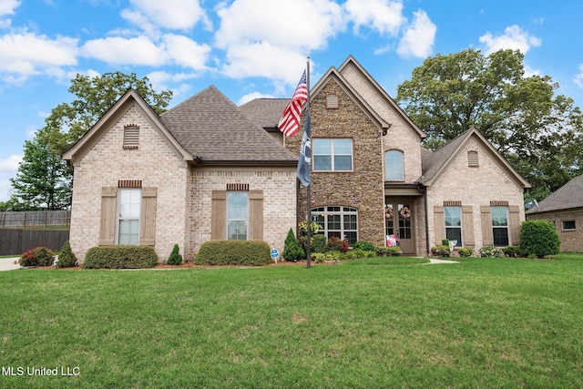 view of front of house with roof with shingles, fence, a front yard, and brick siding