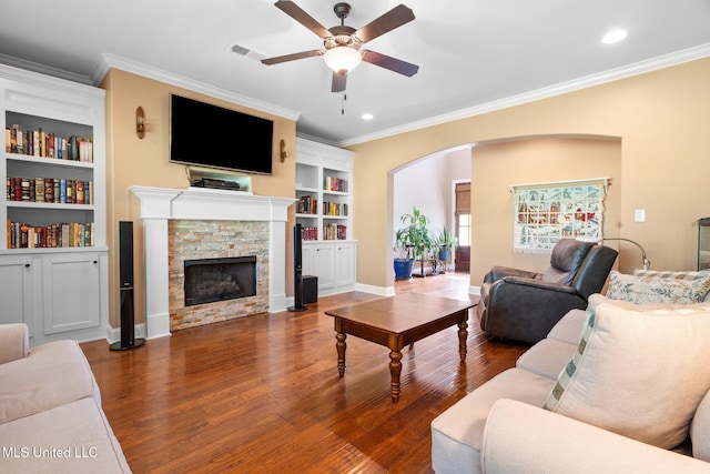 living area featuring ceiling fan, arched walkways, a stone fireplace, visible vents, and ornamental molding