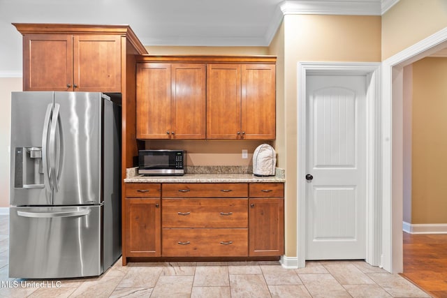 kitchen featuring crown molding, light stone counters, stainless steel fridge with ice dispenser, brown cabinetry, and baseboards
