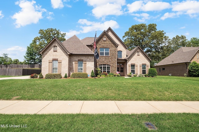 french country inspired facade with brick siding, a front lawn, and fence
