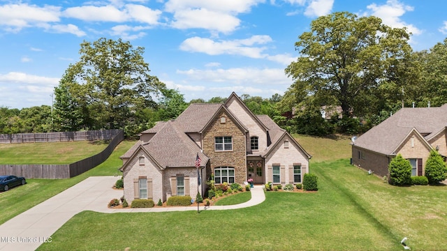 french provincial home with brick siding, fence, stone siding, and a front yard