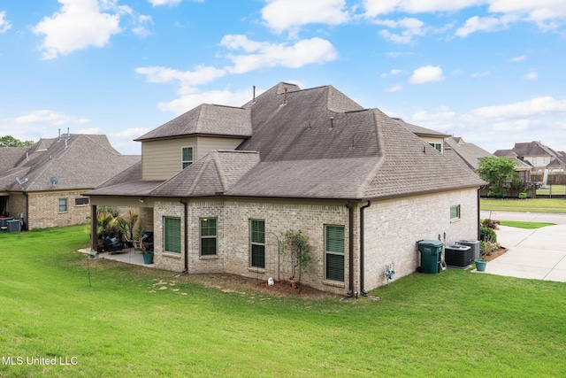 rear view of house featuring cooling unit, roof with shingles, brick siding, a patio area, and a lawn