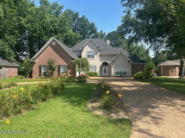 709 Oak Trl, Canton, MS 39046 - traditional-style house featuring a front yard, a chimney, stucco siding, and concrete driveway