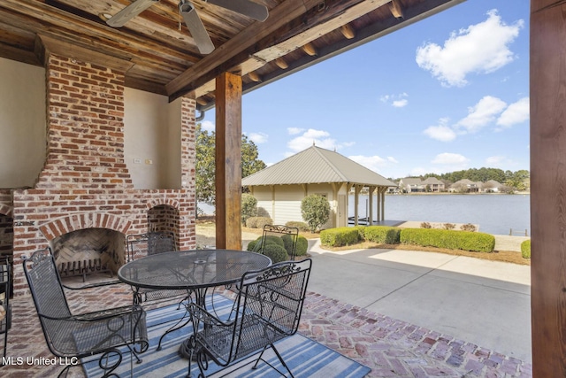 view of patio with outdoor dining area, a water view, ceiling fan, and an outdoor brick fireplace